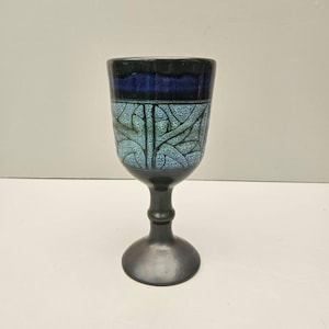 May include: A ceramic goblet with a dark blue rim and base, and a light blue and black patterned design on the cup. The goblet has a stem and a round base. The cup has a textured surface.