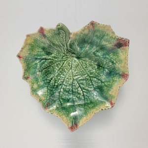 May include: A green ceramic leaf-shaped serving dish with a textured surface and a raised stem. The dish has a light green and yellow glaze with red accents.