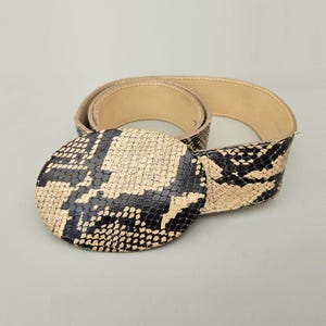 May include: A brown and black snakeskin belt with a large, round, snakeskin buckle.