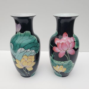 May include: A pair of black ceramic vases with a floral design. The vases are decorated with pink, yellow, and green lotus flowers and leaves.