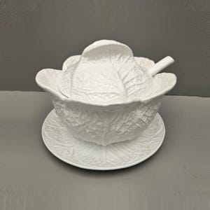 May include: White ceramic serving bowl shaped like a cabbage, with a lid and a matching plate. The bowl and plate feature realistic cabbage leaf textures.