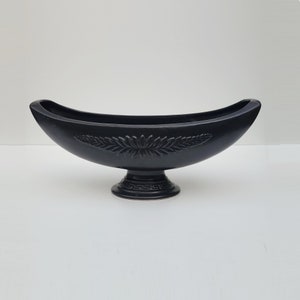 May include: A black ceramic bowl with a leaf design and a pedestal base. The bowl is shaped like a canoe and has a glossy finish.