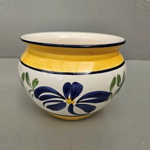 May include: A round ceramic planter with a yellow band and a white base. The planter is decorated with blue floral designs and green leaves. The rim is dark blue. Suitable for indoor or outdoor use. Measures approximately 20 cm in diameter.