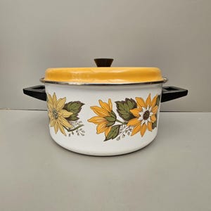 May include: White enamel pot with a yellow lid and sunflower design. The pot has two black handles.