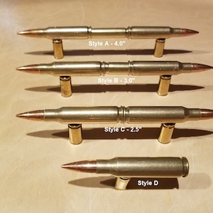 May include: Four different styles of brass bullet shell cabinet door pulls. The pulls are 4.0 inches, 3.0 inches, 2.5 inches, and one style is not measured.  "Style A - 4.0", "Style B - 3.0", "Style C - 2.5", and "Style D" are labeled below each pull.