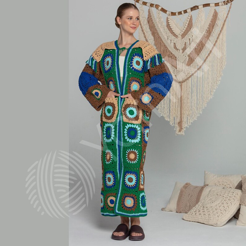 May include: A long, open-front crochet cardigan in a patchwork design. The cardigan features squares in shades of green, blue, brown, and tan. The sleeves are long and wide, and the cardigan reaches to the ankles. The woman is wearing brown sandals.