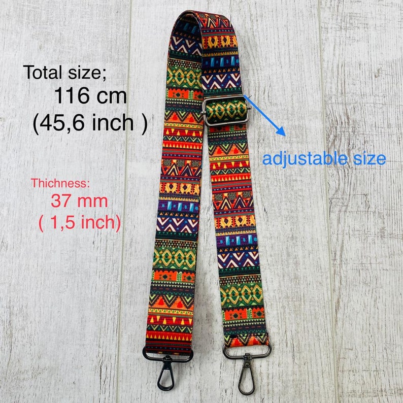May include: An adjustable bag strap featuring a vibrant, multi-colored geometric pattern in red, orange, yellow, green, blue, and black. The strap has a total length of 45.6 inches, a width of 1.5 inches, and includes metal swivel hooks at both ends.