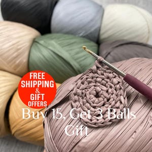 May include: A collection of raffia yarn balls in various colors including black, grey, cream, beige, olive green, and mauve. A metal crochet hook with a mauve handle is inserted into a circular mauve crochet piece resting on a large yarn ball.