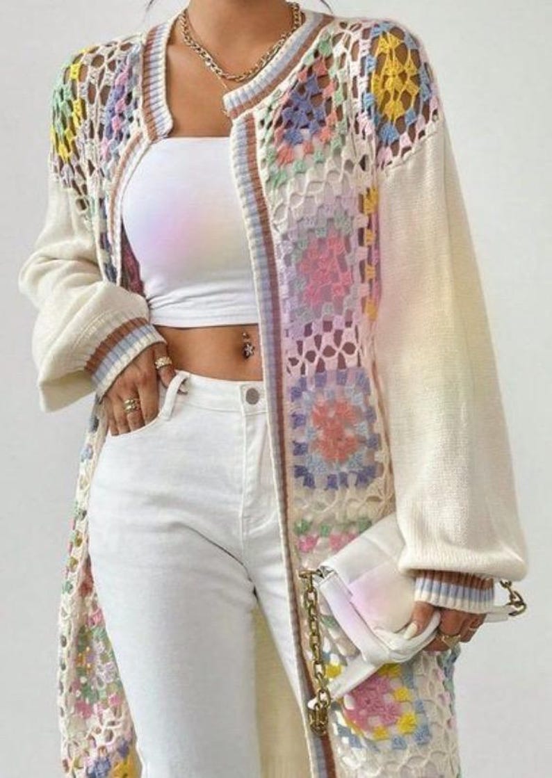 May include: A long-sleeved open-front cardigan featuring a cream-colored knit base with multicolored crochet granny square panels, paired with a white tube top, white jeans, and a white quilted handbag with a gold chain strap.