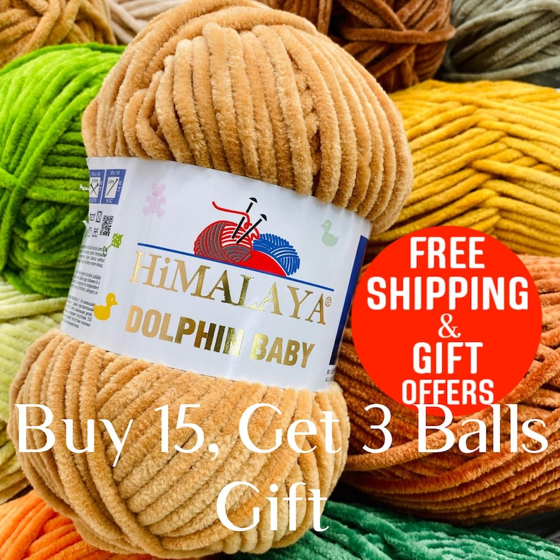May include: A close-up of a ball of tan Himalaya Dolphin Baby yarn. The label features the brand name and a logo with knitting needles and yarn. The text "Buy 15, Get 3 Balls Gift" is also visible.