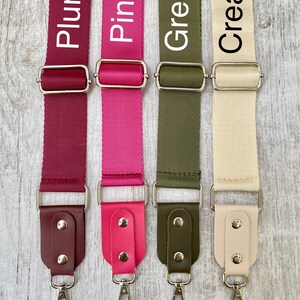 May include: Four adjustable bag straps in plum, pink, olive green, and cream. Each strap features a woven nylon webbing section, a silver-toned metal slider, and a faux leather end tab secured with two silver rivets and a swivel lobster clasp.
