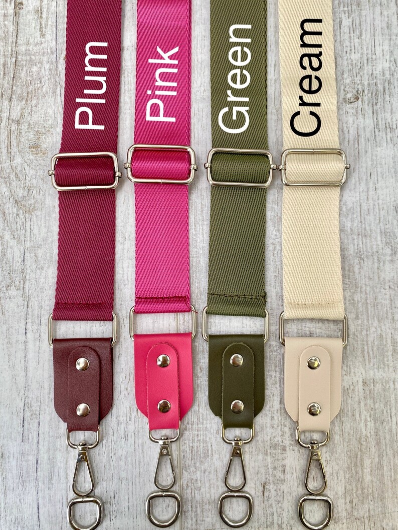 May include: Four adjustable bag straps in plum, pink, olive green, and cream. Each strap features a woven nylon webbing section, a silver-toned metal slider, and a faux leather end tab secured with two silver rivets and a swivel lobster clasp.