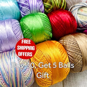 May include: A collection of multiple balls of shiny embroidery thread in various solid and variegated colours including light blue, purple, green, red, gold, and tan, arranged in a cluster with a smooth, tightly wound texture and sheen.