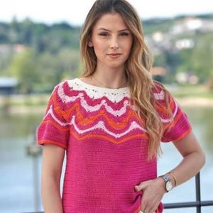 May include: A short-sleeved crochet top featuring a vibrant fuchsia base with a decorative yoke. The yoke displays a wavy, multi-colored pattern in shades of white, light pink, and bright orange, finished with a scalloped white neckline edge.