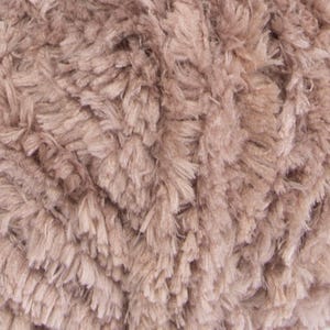 May include: A close-up view of a ball of yarn featuring a soft, shaggy, and textured appearance. The yarn is a solid, muted taupe or light brownish-gray color, characterized by numerous fine, fuzzy fibers that create a dense and plush surface.