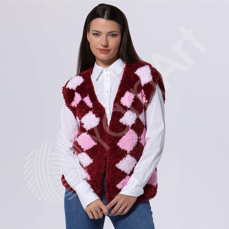 May include: A sleeveless vest featuring a fuzzy, textured argyle pattern in deep burgundy and light pink. The vest has a V-neckline and is worn over a crisp white button-down shirt with long sleeves and blue denim jeans, creating a layered look.