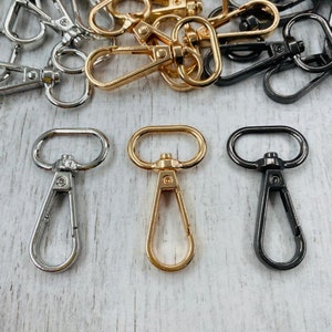 May include: Three metal swivel clasps in silver, gold, and black. The clasps are a common hardware finding for bags, purses, and other accessories.