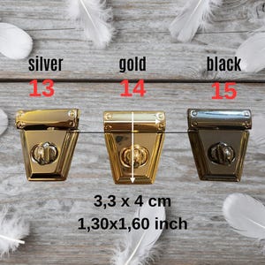 May include: Three metal purse clasps in gold, silver, and black, each with a decorative lock. The clasps measure 3.3 x 4 cm. White feathers are scattered around the clasps on a wooden surface.