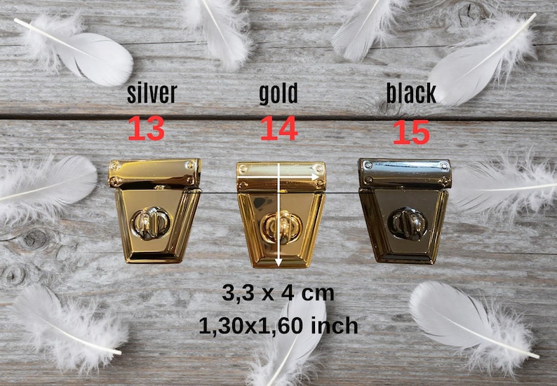 May include: Three metal purse clasps in gold, silver, and black, each with a decorative lock. The clasps measure 3.3 x 4 cm. White feathers are scattered around the clasps on a wooden surface.