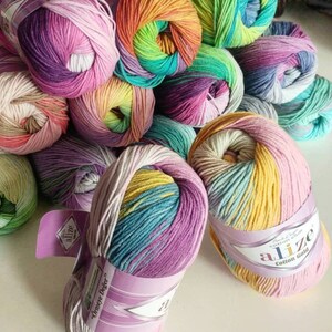 May include: A collection of multi-colored yarn skeins featuring variegated gradients of pink, purple, yellow, green, and blue. Each skein is wrapped in a paper label with the text Alize Cotton Gold and &Ouml;rmeye Değer printed on the front.