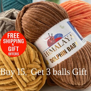 May include: Close-up of several balls of Himalaya Dolphin Baby yarn in various colors, including brown, orange, teal, and yellow. The brown yarn ball is in focus, with a label that reads "Himalaya Dolphin Baby." The yarn has a soft, velvety texture.