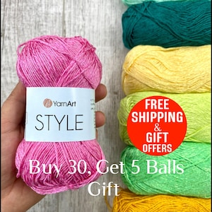 May include: A ball of pink YarnArt STYLE yarn is held in a hand, with the brand name and product name visible on the label. Several other balls of yarn in shades of green and yellow are stacked in the background. The text "Buy 30, Get 5 Balls Gift" is also visible.