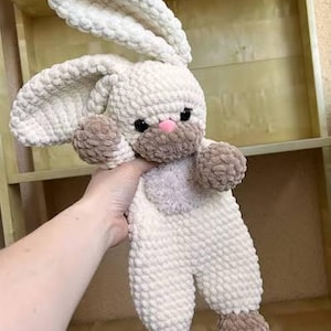 May include: A handmade, plush bunny toy in cream, brown, and pink. The bunny has long, floppy ears, a pink nose, and black eyes. The toy is made of a soft, textured material, and the arms and feet are a darker brown color.
