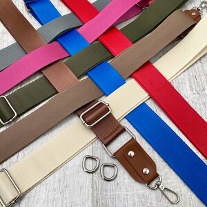 May include: A collection of adjustable bag straps in various colors including red, blue, olive green, brown, pink, gray, and cream. Each strap features silver-toned metal hardware, including sliders and swivel lobster clasps, with some straps featuring brown faux leather accents.