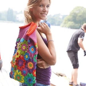 May include: A handmade crochet bag featuring a vibrant floral pattern with multi-colored yarn motifs in shades of red, orange, yellow, green, blue, and purple. The bag has a solid pink top section and a bright orange interior lining visible at the opening.