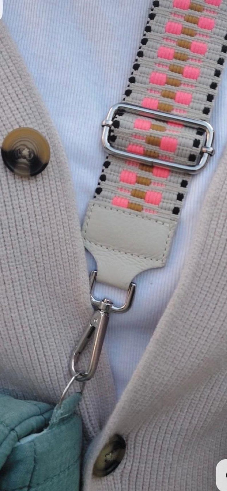 May include: A woven bag strap featuring a pattern of neon pink, tan, and black rectangular blocks on a light beige background. The strap includes a silver metal adjustable slider, a light beige leather tab, and a silver metal lobster clasp.