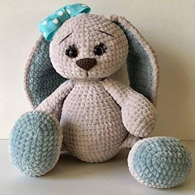 May include: A handmade plush bunny with a light gray body, blue accents, and a blue bow with white polka dots. The bunny has long ears, a brown nose, and black eyes. The bunny is a soft, cuddly toy.