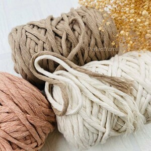 Pu&ograve; includere: Tre matasse di corda di cotone intrecciato spesso nei toni del beige, crema e rosa antico. Il filato presenta una consistenza morbida e tessuta con una struttura intrecciata visibile. Il testo PerfectYarns &egrave; stampato in piccole lettere scure sul cordino beige.