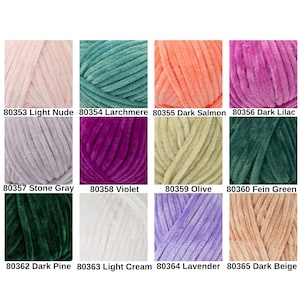 May include: A collection of twelve skeins of plush yarn in various colors. Colors include light nude, teal, salmon, dark lilac, stone gray, violet, olive, and green. Each skein is labeled with a color name and a product number.
