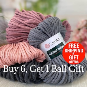 May include: Close-up of several balls of YarnArt Macrame Braided yarn in shades of gray and pink. The image includes text that reads "Buy 6, Get 1 Ball Gift". The yarn is tightly wound and appears soft.
