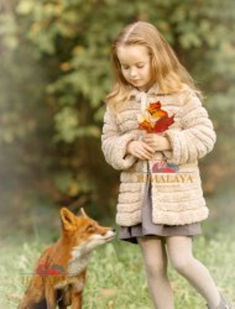 May include: A child with long blonde hair wears a beige textured jacket over a grey dress, holding a cluster of autumn leaves. A red fox stands on the grass nearby. The word HIMALAYA is printed in gold on the front of the jacket.