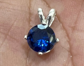 May include: A silver pendant with a round, dark blue gemstone.