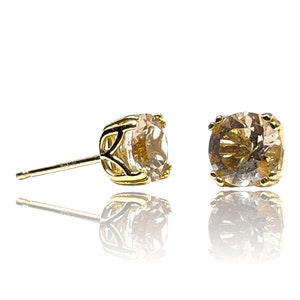 May include: A pair of gold stud earrings with a round, clear, faceted gemstone in each setting.