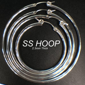 May include: Four silver hoop earrings of different sizes, stacked on top of each other. The earrings are 2.3mm thick and are made of stainless steel.  SS HOOP 2.3mm Thick is printed on the earrings.