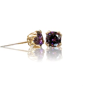 May include: A pair of gold stud earrings with purple gemstones. The earrings have a delicate, ornate design.