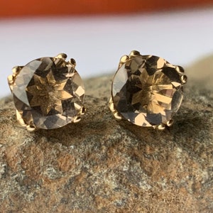 May include: A pair of gold stud earrings with a light brown, faceted gemstone in each.