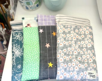 May include: Four fabric pouches with different patterns. The pouches are lined up on a white surface. The pouch on the right has a white daisy pattern and the text "Pine + Paper" on the bottom right corner.
