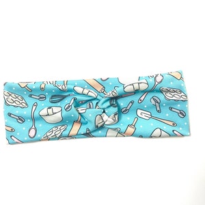 May include: A light blue headband with a white polka dot pattern and a repeating pattern of baking tools, including a rolling pin, whisk, measuring cups, and a spatula.