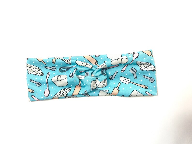 May include: A light blue headband with a white polka dot pattern and a repeating pattern of baking tools, including a rolling pin, whisk, measuring cups, and a spatula.