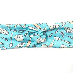 May include: A light blue headband with a white background and a pattern of various baking tools, including rolling pins, whisks, spatulas, and measuring cups.