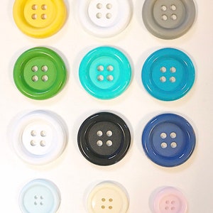 Könnte beinhalten: Sortiment von 12 bunten Knöpfen mit jeweils vier Löchern. Die Knöpfe sind in verschiedenen Farben, darunter Gelb, Weiß, Grau, Grün, Türkis, Blau, Schwarz, Hellblau, Creme und Rosa.