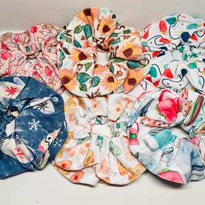 May include: A set of 7 colorful scrunchies with various patterns, including floral, winter, and kitchen-themed designs. The scrunchies are made of soft fabric and are perfect for holding hair in place.