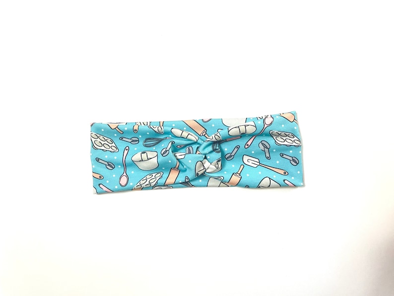 May include: A light blue headband with a pattern of baking tools and white polka dots. The headband is knotted in the center.