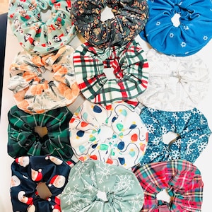 May include: A collection of 10 colorful scrunchies with various holiday-themed patterns, including snowflakes, plaid, and Christmas lights.