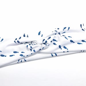 Pode incluir: Faixa de cabeça branca com um padrão de pegadas azuis. A faixa de cabeça é feita de um tecido macio e elástico, perfeita para adicionar um toque de fantasia a qualquer roupa.