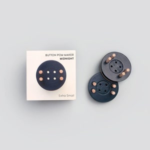 May include: A set of three black button pom pom makers in the "Midnight" color. The makers are extra small and are shown on a white background with a product label that reads "Button Pom Maker Midnight Extra Small".